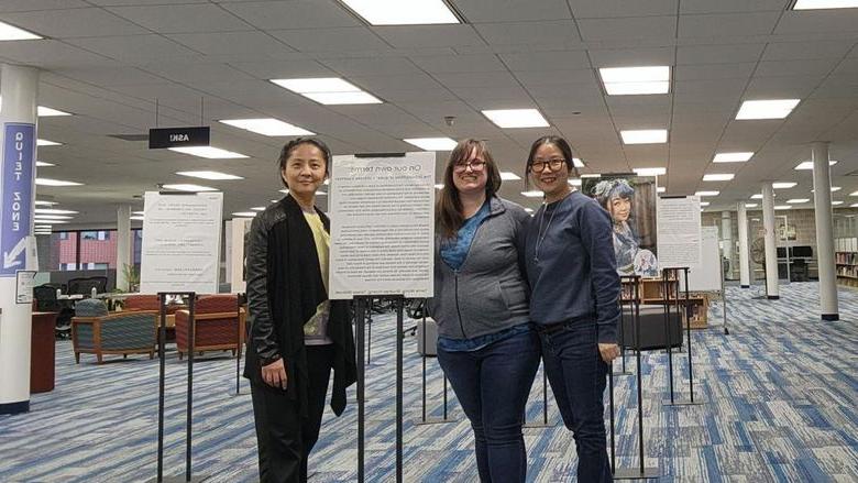 Three women standing in front of sign for exhibit