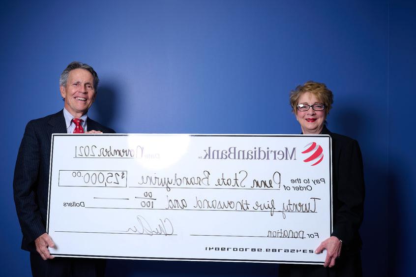 Meridian CEO Chris 亚那 with 宾州州立大学白兰地酒 总理 Marilyn 井 stand in front of a blue wall holding a large white check. 